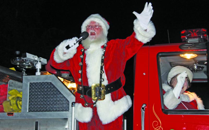 Santa Claus on the back of a firetruck.