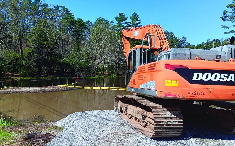 An excavator sits at the ready next to Mirror Lake where the yellow boundary lines for dredging have been put in place.