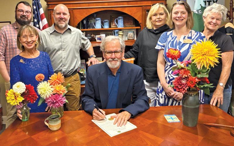 Highlands Mayor Patrick Taylor signs a proclamation designating the week of Sept. 1, as “Dahlia Week. Front row: Kim Daughtry, Taylor, and Bianca Mitchell. Back row: Zach Rogers, Billy Love, Peggy Boruchow Arnette, and Lisa Dailey.