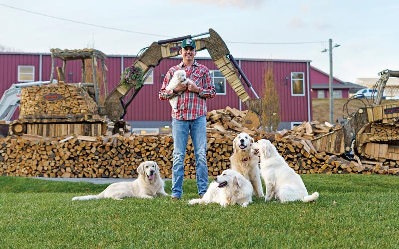 Joshua Crawford, accompanied by his golden retrievers, shows off his skid steer and crawler excavator firewood designs at the 2025 Cashiers Festival of Trees.  |  Photo courtesy of Chelsea Cronkite