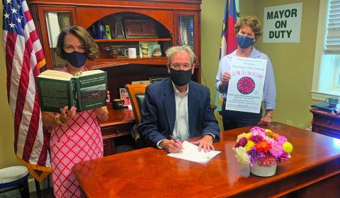 Highlands Mayor Patrick Taylor signs a proclamation celebrating this weekend’s 10th annual Dahlia Festival. From left, Kim Daugherty holding the book, Taylor and Lisa Dailey.