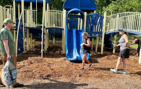 Volunteers spread fresh mulch under the playground equipment at Highlands School on Aug. 12.