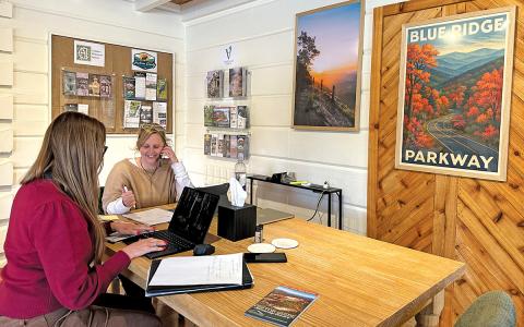 Visitor Center host Heather Dalton and Amanda Bradley work at the newly added farm tables in front of original artwork and photographs.  |  Photos by Mitch Stone/Staff