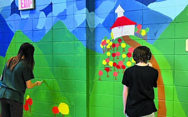 A pair of Highlands students work on a hallway mural as part of art class.
